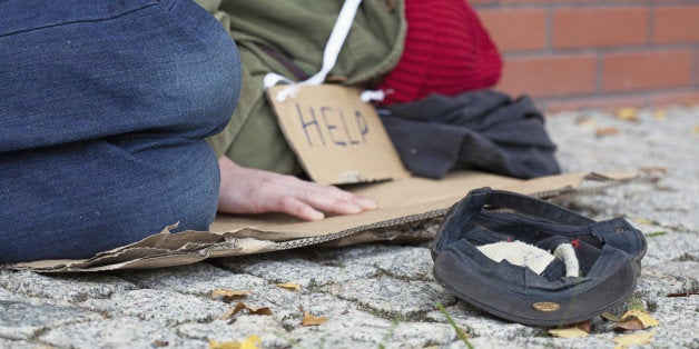 Beggar falling asleep on the street with a cap for collecting money