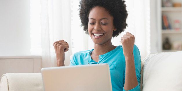 African American woman cheering at laptop on sofa