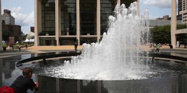 NEW YORK, NY - JULY 29: A boy lies in the cool mist from a fountain in front of the Metropolitan Opera on July 29, 2014 at L