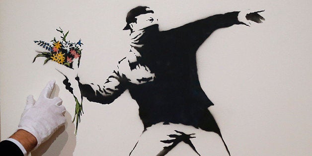 A Bonhams employee points at the colored detail of a spray paint work by urban artist Banksy at Bonhams auction house in London, Monday, June 24, 2013. The work Love Is In The Air is expected to fetch 100,000 pounds (US$150,000, euro120,000) and will be offered for sale by Bonhams on June 27.(AP Photo/Frank Augstein)