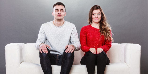Shy woman and man sitting on sofa couch next each other. First date. Attractive girl and handsome guy meeting dating and tryi