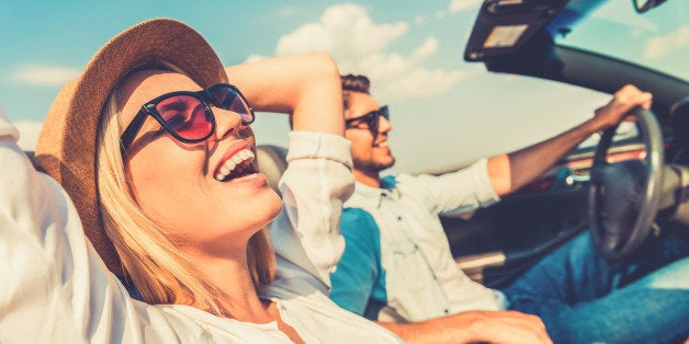 Side view of joyful young woman relaxing on the front seat while her boyfriend sitting near and driving their convertible