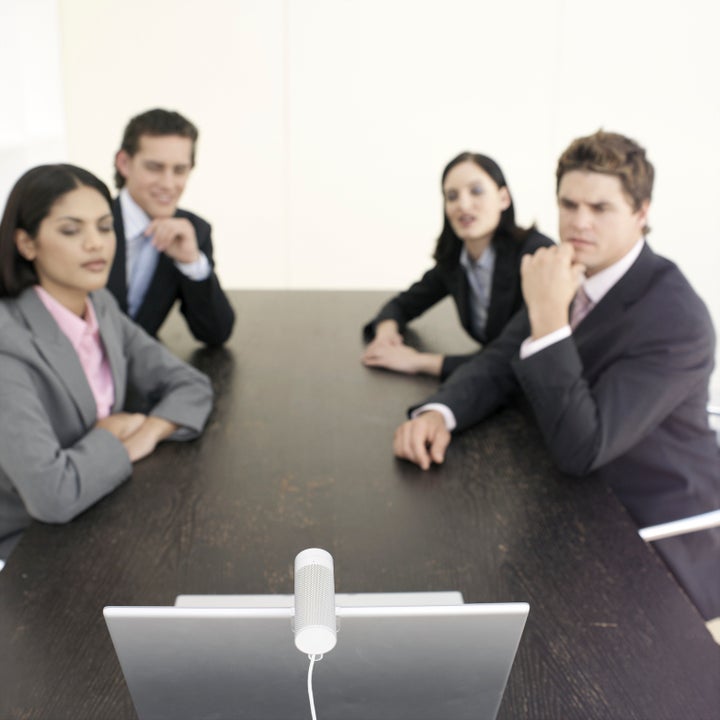 Four business people sitting at desk having video conference (focus on foreground)