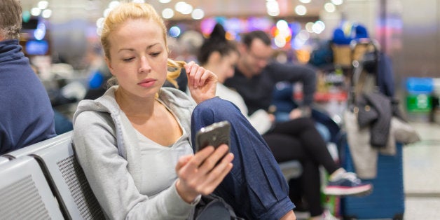 Casual blond young woman using her cell phone while waiting to board a plane at the departure gates. Wireless network hotspot enabling people to access internet conection. Public transport.