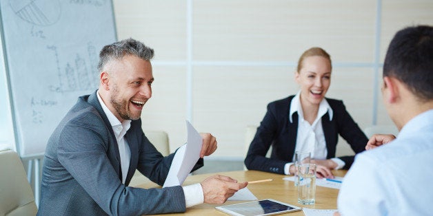 Laughing businessman with paper talking to colleagues in office