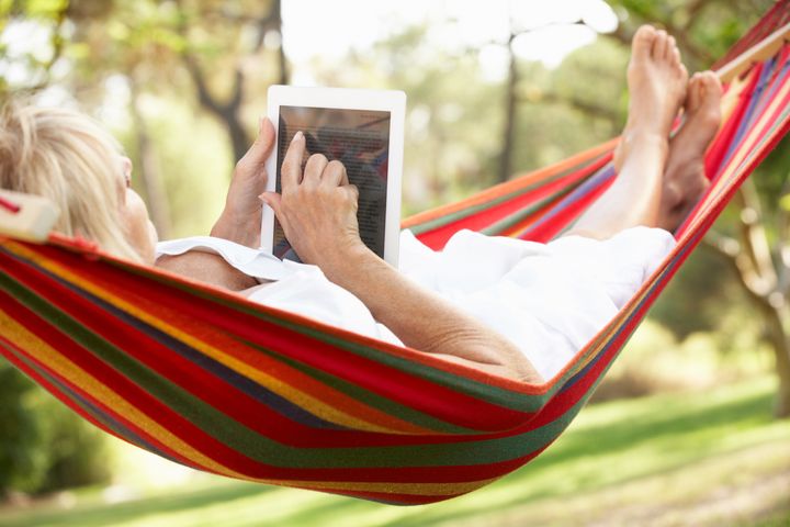 Senior Woman Relaxing In Hammock With E-Book
