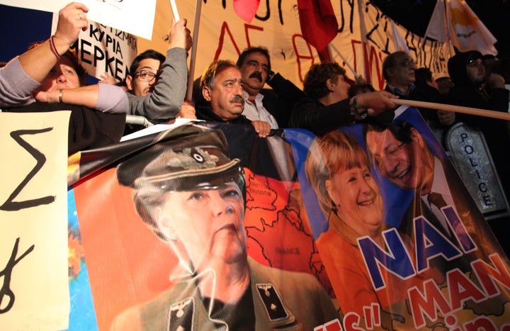 Cypriot protestors wave banners picturing German Chancellor Angela Merkel (C) and Cypriot President Nicos Anastasiades (R) during a demonstration against an EU bailout deal outside the parliament in the capital, Nicosia, on March 19, 2013. The speaker of the Cypriot parliament urged MPs to say 'no to blackmail' in a vote on a eurozone bailout aimed at saving the Mediterranean island from bankruptcy. AFP PHOTO/BARBARA LABORDE (Photo credit should read BARBARA LABORDE/AFP/Getty Images)