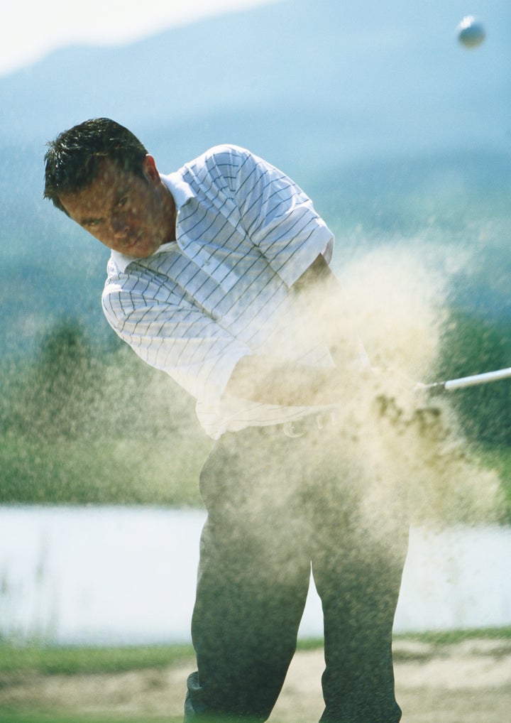 Golfer, mid-swing in sand trap, with sand in mid-air