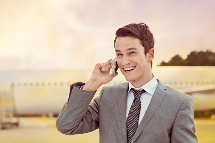 Outdoor portrait of excited young adult businessman standing in front of airplane and talking on a mobile phone.