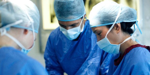Surgeons in hospital scrubs operating during surgery - focus on female surgeon