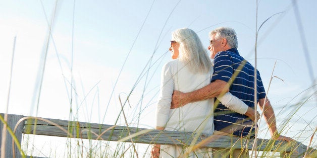 A retired man (70 years old) holding and standing next to a woman (60 years old) with their backs to the camera watching the sunset on top of a hill with water, green trees and blue sky in the background on location at Longboat Key Florida for Retirement, Vacation, Commitment, Growing Old Together, Wellness, Active, Happiness, Escape, Freedom, Vacation, Getting Away From It All, Relationship, Companionship, Grandparents