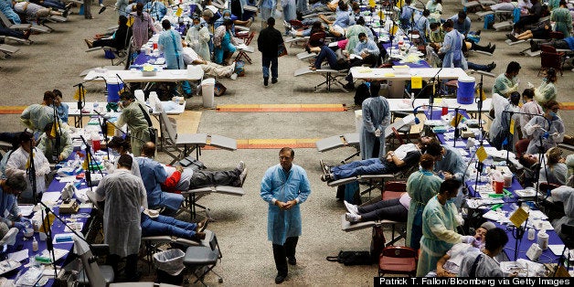 Dr. Dave Campbell, associate clinical professor at University of Southern California (USC), center, walks past patients receiving medical attention at a Care Harbor LA free health clinic for the uninsured and underinsured at the Los Angeles Sports Arena in Los Angeles, California, U.S., on Thursday, Sept. 27, 2012. Almost 16 percent of the U.S. population, or 48.6 million people, lack health insurance. Photographer: Patrick T. Fallon/Bloomberg via Getty Images