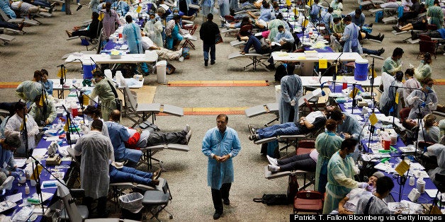 Dr. Dave Campbell, associate clinical professor at University of Southern California (USC), center, walks past patients receiving medical attention at a Care Harbor LA free health clinic for the uninsured and underinsured at the Los Angeles Sports Arena in Los Angeles, California, U.S., on Thursday, Sept. 27, 2012. Almost 16 percent of the U.S. population, or 48.6 million people, lack health insurance. Photographer: Patrick T. Fallon/Bloomberg via Getty Images 