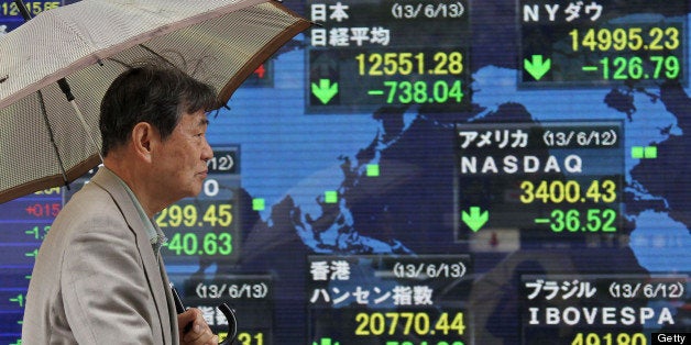 A pedestrian with an umbrella walks past an electronic stock board in Tokyo, Japan, on Thursday, June 13, 2013. Japanese stocks plunged, with the Nikkei 225 Stock Average entering a bear market at the close, as the yen rose to its strongest against the dollar in two months. All shares on the gauge fell for the second time this year. Photographer: Junko Kimura/Bloomberg via Getty Images