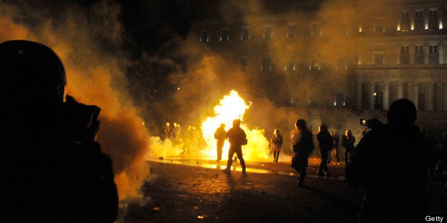 A petrol bomb explodes amid tear gas used by police to disperse demonstrators during clashes between protesters and riot police outside the Greek parliament in Athens on February 12, 2012. Greek police fired tear gas at petrol bomb-throwing protesters outside parliament, where tens of thousands had massed in a rally against austerity plans being debated by lawmakers. Police said some 80,000 protesters had gathered outside the building where debate on the plan imposed by the country's international creditors -- the EU, the IMF and the European Central Bank -- was ongoing before a late-night vote. AFP PHOTO / LOUISA GOULIAMAKI (Photo credit should read LOUISA GOULIAMAKI/AFP/Getty Images)