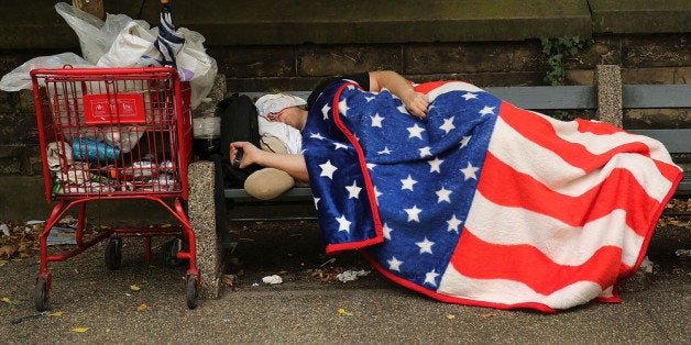 NEW YORK, NY - SEPTEMBER 10: A homeless man sleeps under an American Flag blanket on a park bench on September 10, 2013 in the Brooklyn borough of New York City. As of June 2013, there were an all-time record of 50,900 homeless people, including 12,100 homeless families with 21,300 homeless children homeless in New York City. (Photo by Spencer Platt/Getty Images)