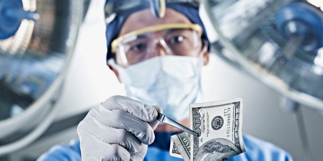 Portrait of surgeon holding one hundred dollar bill under surgical lights
