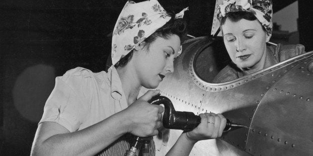 circa 1943: One American female worker drives rivets into an aircraft while another sits in the cockpit on the US home front during World War II. They wear aprons and their hair tucked into scarves. Women who went to work in industries to aid the war effort became known under the moniker 'Rosie the Riveter'. (Photo by Harold M. Lambert/Lambert/Getty Images)