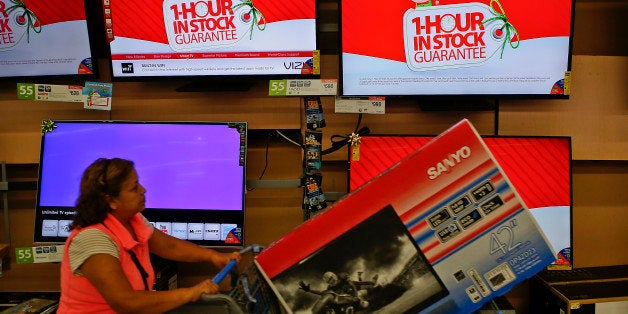 A customer pushes a shopping cart with a television as screens show advertisements for the Black Friday 1 Hour In Stock Guarantee at a Wal-Mart Stores Inc. location ahead of Black Friday in Los Angeles, California, U.S., on Tuesday, Nov. 26, 2013. Wal-Mart Stores Inc. said Doug McMillon, head of its international business, will replace Mike Duke as chief executive officer when he retires as the world's largest retailer struggles to ignite growth at home and abroad. Photographer: Patrick T. Fallon/Bloomberg via Getty Images