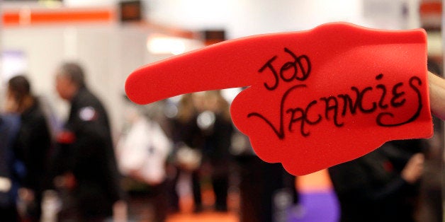 An exhibitor holds a giant red foam hand with the words 'Job Vacancies' at a stand during the Skills London job fair in Londo