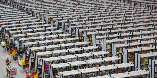 An employee pushes a cart past rows of storage aisles as he processes customer orders ahead of shipping at one of Amazon.com Inc.'s fulfillment centers in Rugeley, U.K., on Monday, Dec. 2, 2013. Online retailers in the U.K. are anticipating their busiest day as shoppers flush with end-of-month pay-checks seek Christmas deals on the Web. Photographer: Simon Dawson/Bloomberg via Getty Images