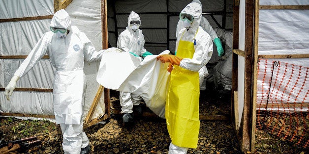 KENEMA, SIERRA LEONE - AUGUST 24: A group of young volunteers wear special uniforms to put the bodies of people, sterilized after dying due to the Ebola virus, to a car ahead of their burials in Kptema graveyard in Kenema, Sierra Leone on August 24, 2014. People work for 6 dollars per a day in burial and sterilizing works in Kenema where the infection of the virus is mostly seen. (Photo by Mohammed Elshamy/Anadolu Agency/Getty Images)