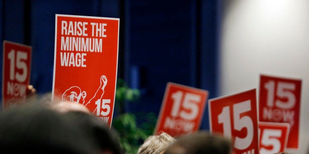 Signs supporting a $15 minimum wage are held up at an inaugural event for new Seattle City Council members, city attorney and may Monday, Jan. 6, 2014, in Seattle. Sawant is a Socialist. (AP Photo/Elaine Thompson)