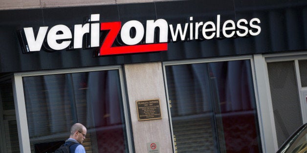 A pedestrian looks at a mobile device as he walks past a Verizon Wireless retail store in Washington, D.C., U.S., on Friday, Oct. 24, 2014. Verizon Communications Inc., the largest U.S. wireless carrier, missed profit estimates on Oct. 21 as more new subscribers took advantage of discounts on devices. Photographer: Andrew Harrer/Bloomberg via Getty Images