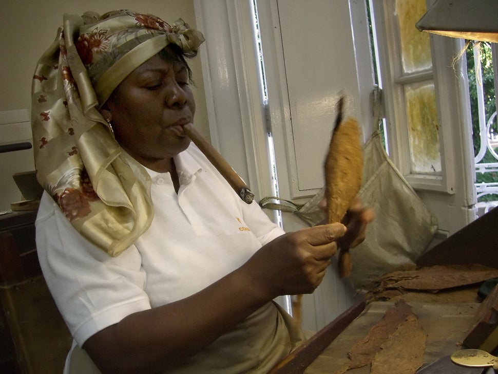 2006 - A cigar roller smokes a cigar while she prepares tobacco leaves at Cuban cigar manufacturer Cohiba's factory.