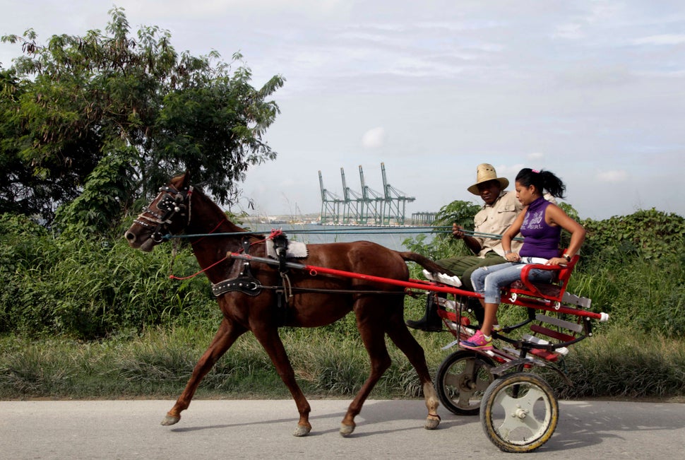 2013 - A man drives a horse drawn carriage past a port under construction in Mariel Bay.
