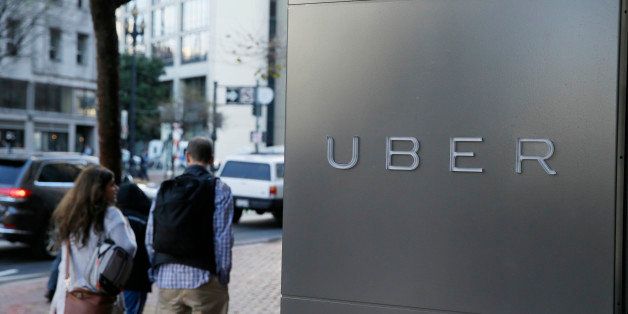 In this photo taken Tuesday, Dec. 16, 2014, a couple walks past the headquarters of Uber in San Francisco. (AP Photo/Eric Risberg)