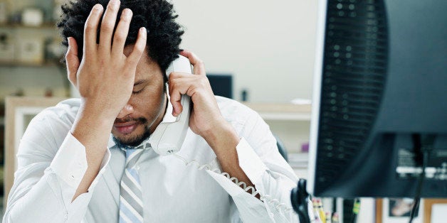 Businessman on phone at desk in office with hand on forehead