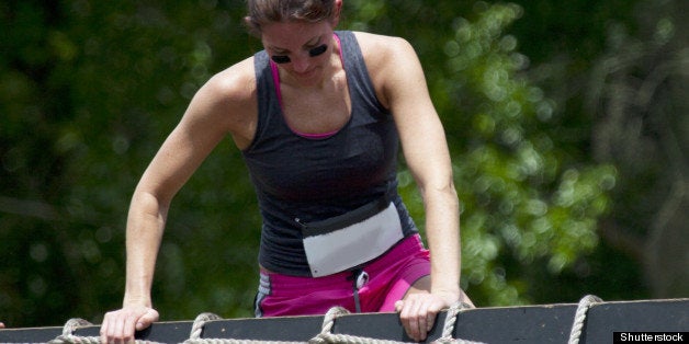 Young woman participant of charity obstacle course climbs up and over the net barrier.