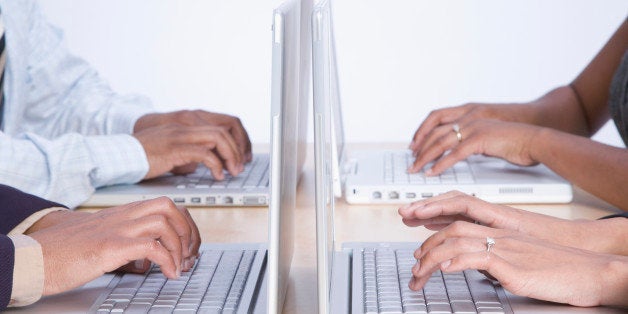 Four business people working on laptop computers, close-up on hands