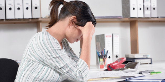 Young pregnant woman sitting at desk looking at document, side view