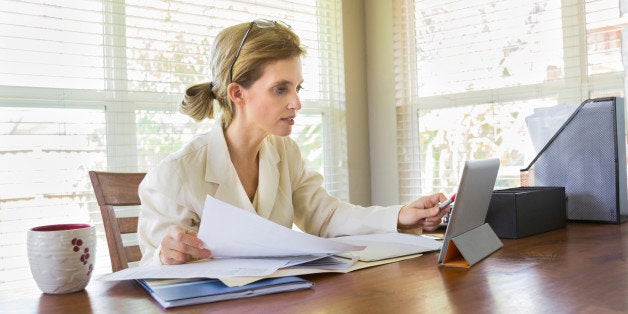 Lifestyle image of a middle-aged woman looking at her tablet while working with documents in her office. Horizontal image