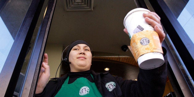 Starbucks barista Alex Igarta hands a coffee drink to a customer from a drive-up window at a store near the company's corporate headquarters Monday, Jan. 26, 2009, in Seattle. Starbucks reported Wednesday that its profits dropped 69 percent in its fiscal first quarter and it plans to close more stores and cut more jobs. (AP Photo/Elaine Thompson)