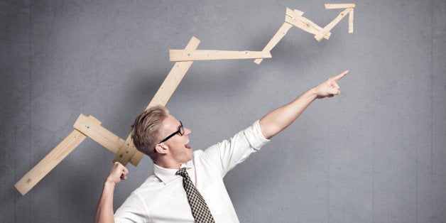 Concept: Successful business trend. Happy talented businessman pointing arm upwards in front of ascending business graph, isolated on grey background.