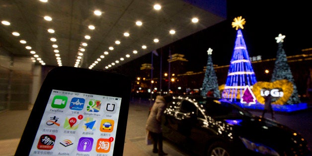 The Uber app is displayed on a phone posed for photos near a woman peering into a car outside a office building in Beijing, Friday, Jan. 9, 2015. China has banned drivers of private cars from offering services through ride-hailing apps, throwing up a new hurdle to Uber Technologies Ltd.'s global expansion. (AP Photo/Ng Han Guan)