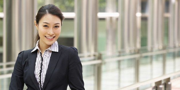 Chinese Businesswoman Working On Tablet Computer Outside Office Looking At Camera Smiling