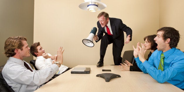 Crazy boss standing on conference table and yelling at employees with megaphone.