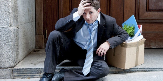 frustrated and sad business man in stress sitting on edgy street corner depressed and desperate, fired from work in crisis asking for help carrying office belongings on cardboard box