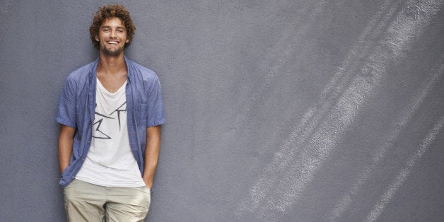 Full-length shot of a handsome young man leaning against a gray wall