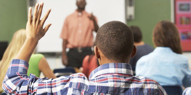 Male Pupil Raising Hand In Class Sitting At Desk