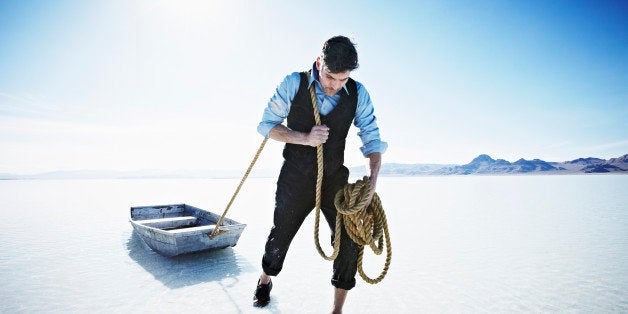 Businessman pulling small boat with rope through shallow water
