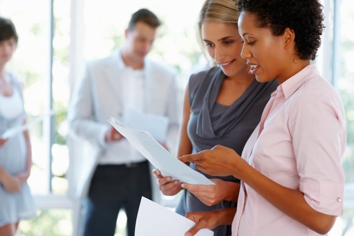 Two business women going through the documents with team in background