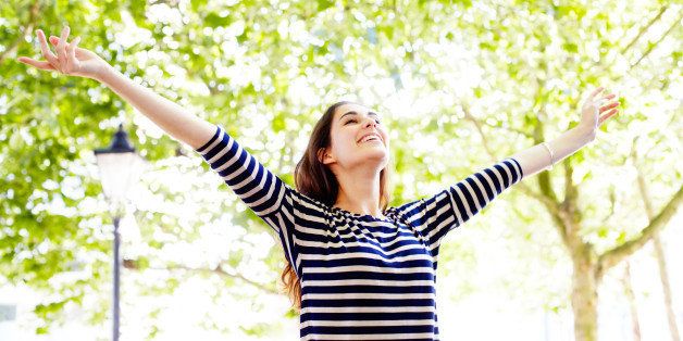 Young woman next to trees with arms in the air