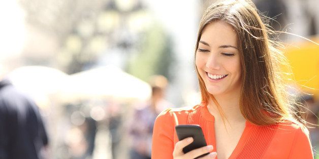 Woman wearing orange shirt texting on the smart phone walking in the street in a sunny day