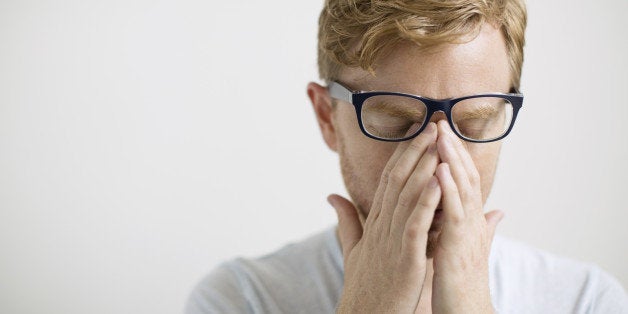 Blonde man rubbing eyes under eyeglasses
