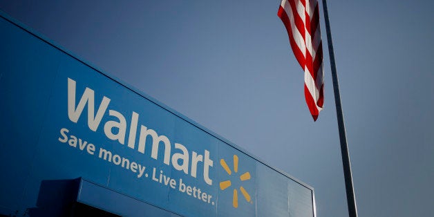 An American flag flies near signage displayed outside of the Wal-Mart Stores Inc. headquarters building in Bentonville, Arkansas, U.S., on Wednesday, July 29, 2015. Wal-Mart Stores Inc. is scheduled to release earnings figured on Aug. 18. Photographer: Luke Sharrett/Bloomberg via Getty Images